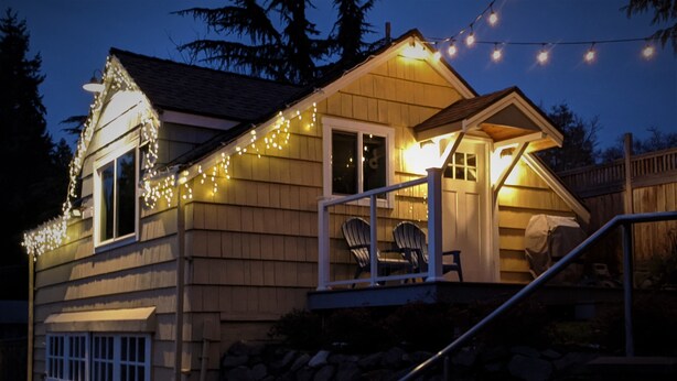 Una casa de madera con luces de cuerda, un porche cubierto y un muro de piedra.
