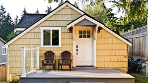 Una pequeña casa de madera con un porche, dos sillas y una puerta.