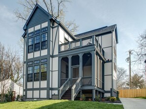 A two-story house with a balcony, large windows, and a staircase leading to the entrance.