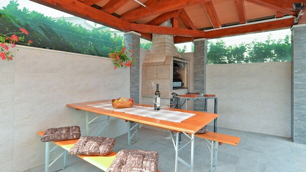 An outdoor patio with a wooden table, benches, and a stone oven.