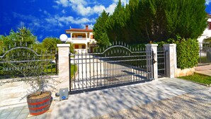 A gated entrance with a metal gate, a potted plant, and a building with a red roof in the background.