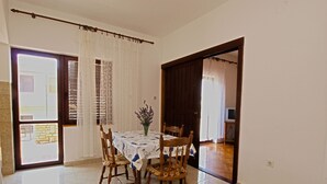 A dining area with a table set for four, wooden chairs, a vase with flowers, and a view through a glass door to an outdoor space. - Apartment 349/808 (Istria - Peroj), 700m from the beach (Peroj)