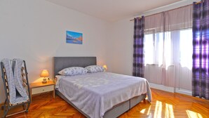 A bedroom with a bed, a nightstand, a lamp, a painting on the wall, and a window with curtains. - Apartment 351/776 (Istria - Fažana), 300m from the beach (Fažana)
