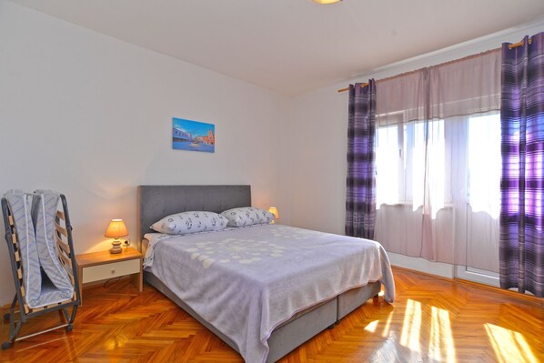 Quarto com cama, mesa de cabeceira, luminária, pintura na parede e janela com cortinas.