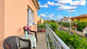 A balcony with a table and chairs, a vase with flowers, and a view of a street with houses and greenery. - Apartment 351/776 (Istria - Fažana), 300m from the beach (Fažana)
