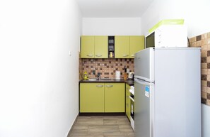 Uma cozinha compacta com armários verdes, micro-ondas e geladeira.