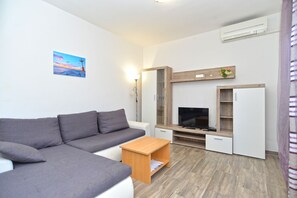 A modern living room with a grey sofa, a wooden coffee table, a TV, and a white refrigerator. - Apartment 351/817 (Istria - Fažana), 300m from the beach (Fažana)