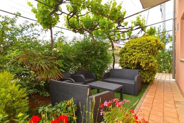 An outdoor patio with wicker furniture, a variety of plants, and a view of the surrounding area.
