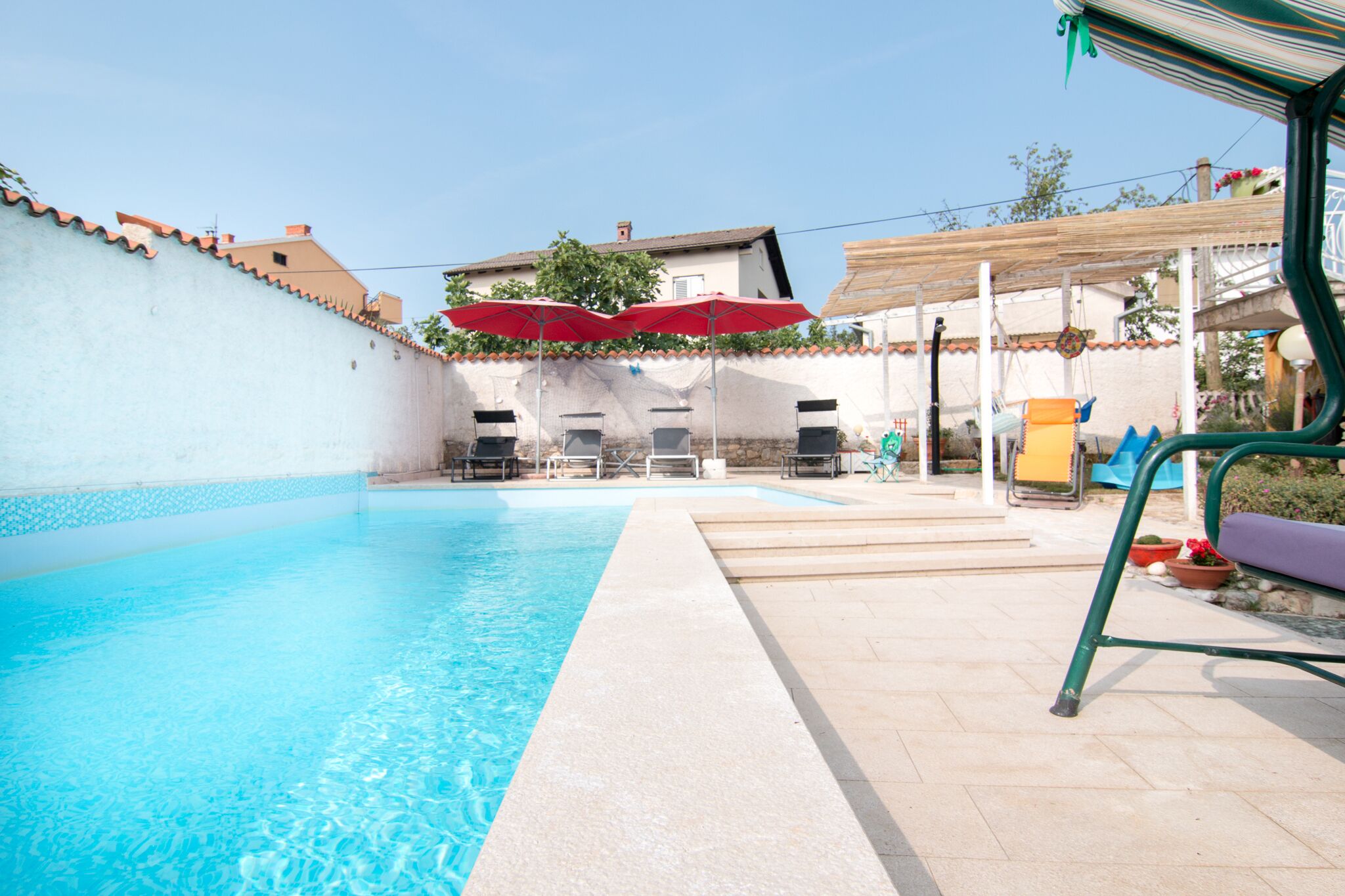 Une piscine à l’eau d’un bleu cristallin, entourée d’une terrasse carrelée et d’un mur blanc.