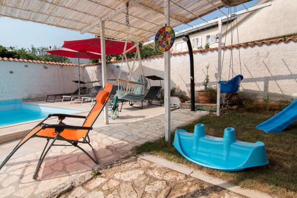 A backyard with a swimming pool, outdoor seating, a hanging swing, and a slide.