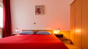 A bedroom with a red bedspread, two pillows, a wooden wardrobe, and two bedside lamps. - Apartment 354/821 (Istria - Valbandon), 950m from the beach (Valbandon)