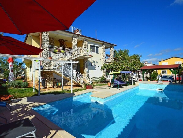 A swimming pool area with a stone building, a balcony, and a covered seating area.