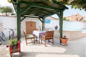 Une terrasse couverte avec une table et des chaises, un vélo et une plante en pot.