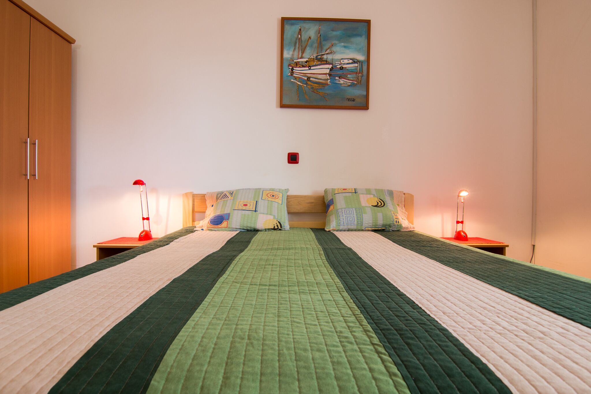 Une chambre à coucher comprenant un lit, deux tables de chevet, une commode, un tableau accroché au mur et une armoire.