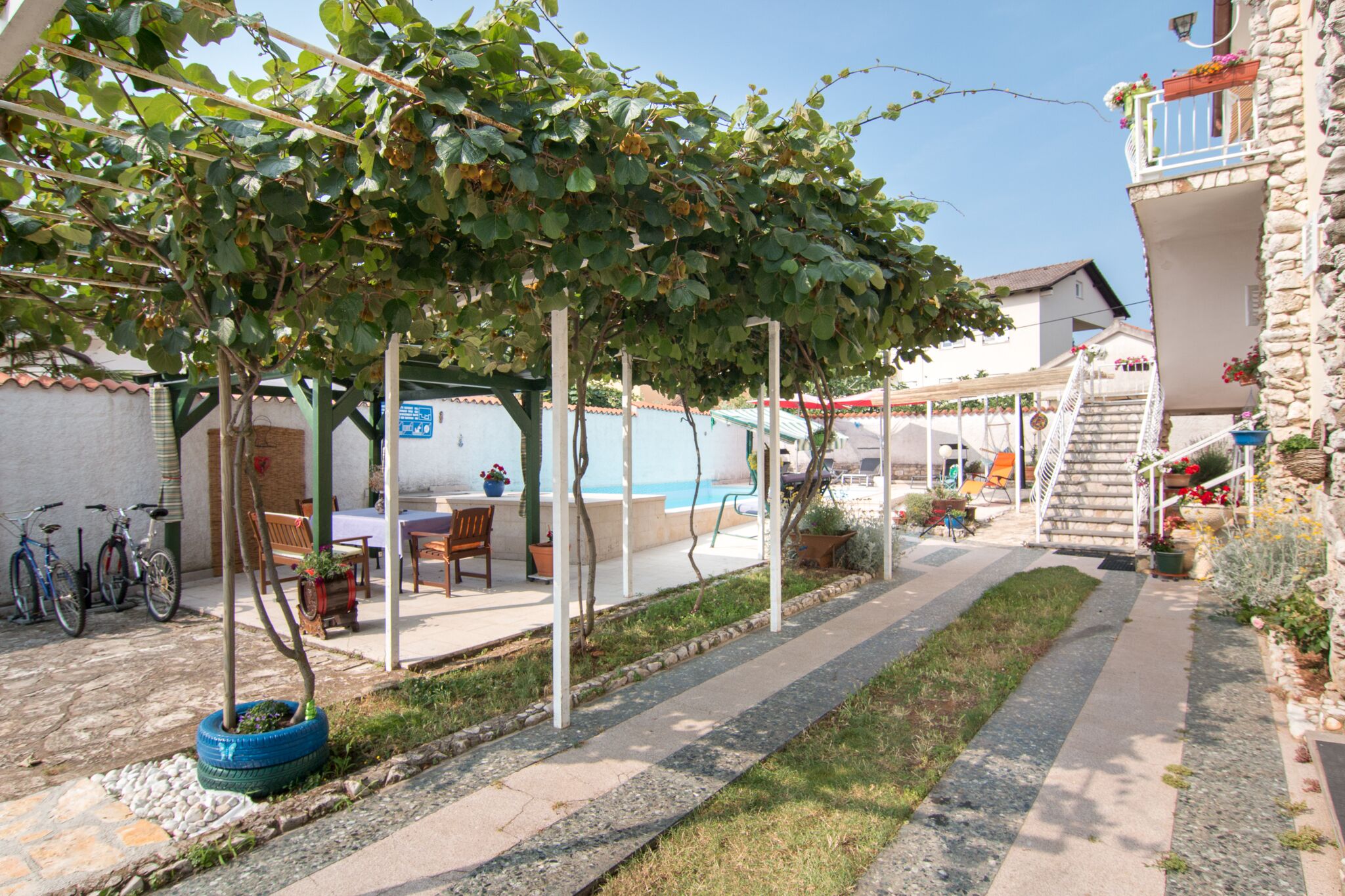 Une cour dotée d’une pergola, d’un espace salon extérieur, d’une piscine et d’un escalier menant à un balcon.