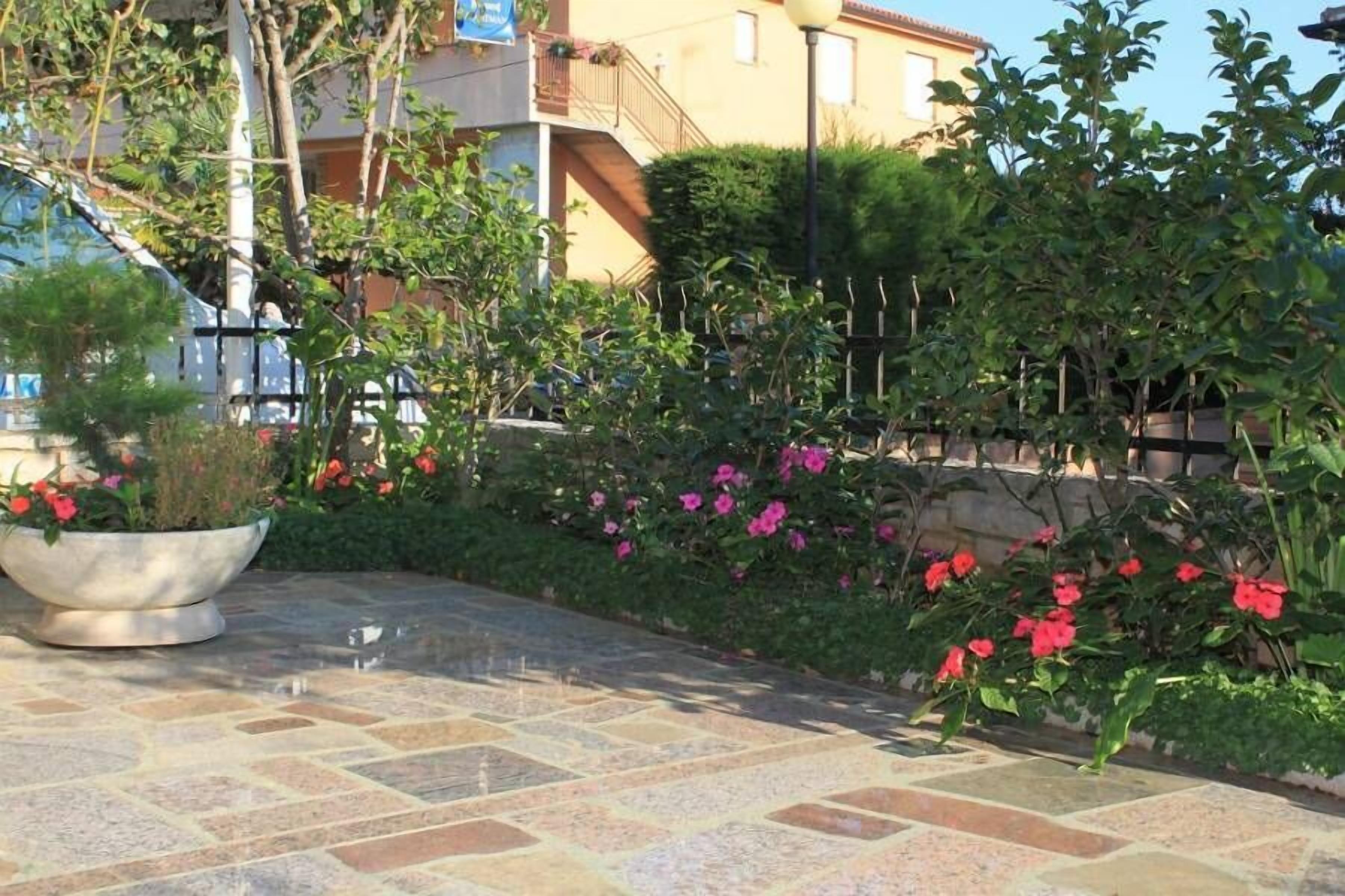 A courtyard with a tiled floor, potted plants, and flowering shrubs.