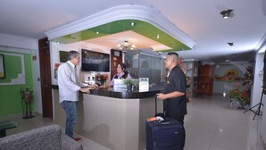 A hotel reception area with a counter, a receptionist, and a guest with luggage. - Hotel Grand Latino Ibague (Ibagué)