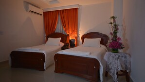 A bedroom with two single beds, an air conditioning unit, a nightstand with a lamp, and a floral arrangement. - Hotel Grand Latino Ibague (Ibagué)