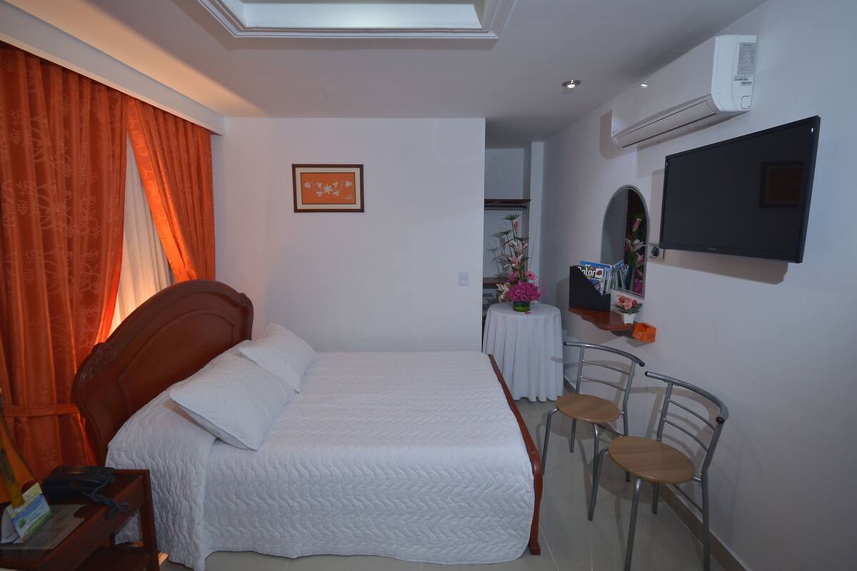 Een hotelkamer met een bed, bureau, stoel, televisie en een kleine tafel met bloemen.