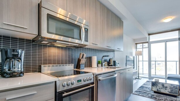 A modern kitchen with stainless steel appliances, a large window, and a minimalist design.