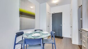 A modern kitchen with a built-in refrigerator, a dining area with a glass table and blue chairs, and a gray door in the background.