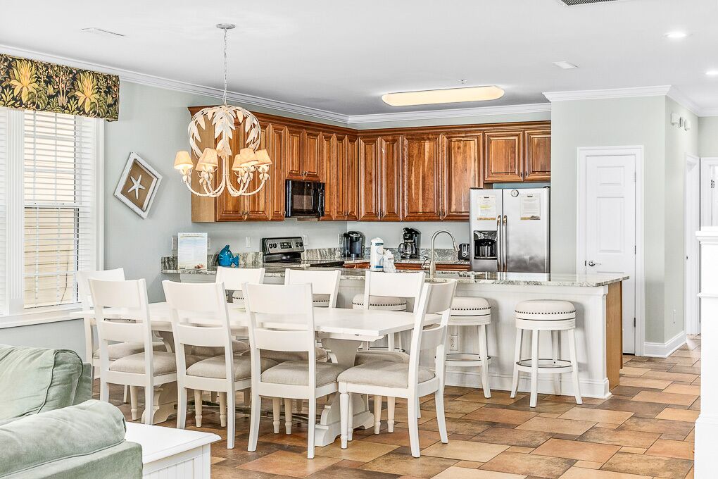 Une cuisine moderne avec des meubles en bois, un îlot central doté de tabourets et un coin repas avec des chaises blanches.