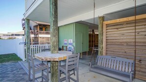 A patio with a wooden table and two chairs, a swing, and a closed garage door. - 6BR Home w/ Private Pool & Ocean Views (Garden City Beach)