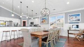 A modern kitchen with white cabinets, a wooden dining table, and bar stools. - 6BR Home w/ Private Pool & Ocean Views (Garden City Beach)