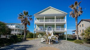 A two-story building with a balcony, surrounded by palm trees and a paved area with a circular pattern. - 6BR Home w/ Private Pool & Ocean Views (Garden City Beach)