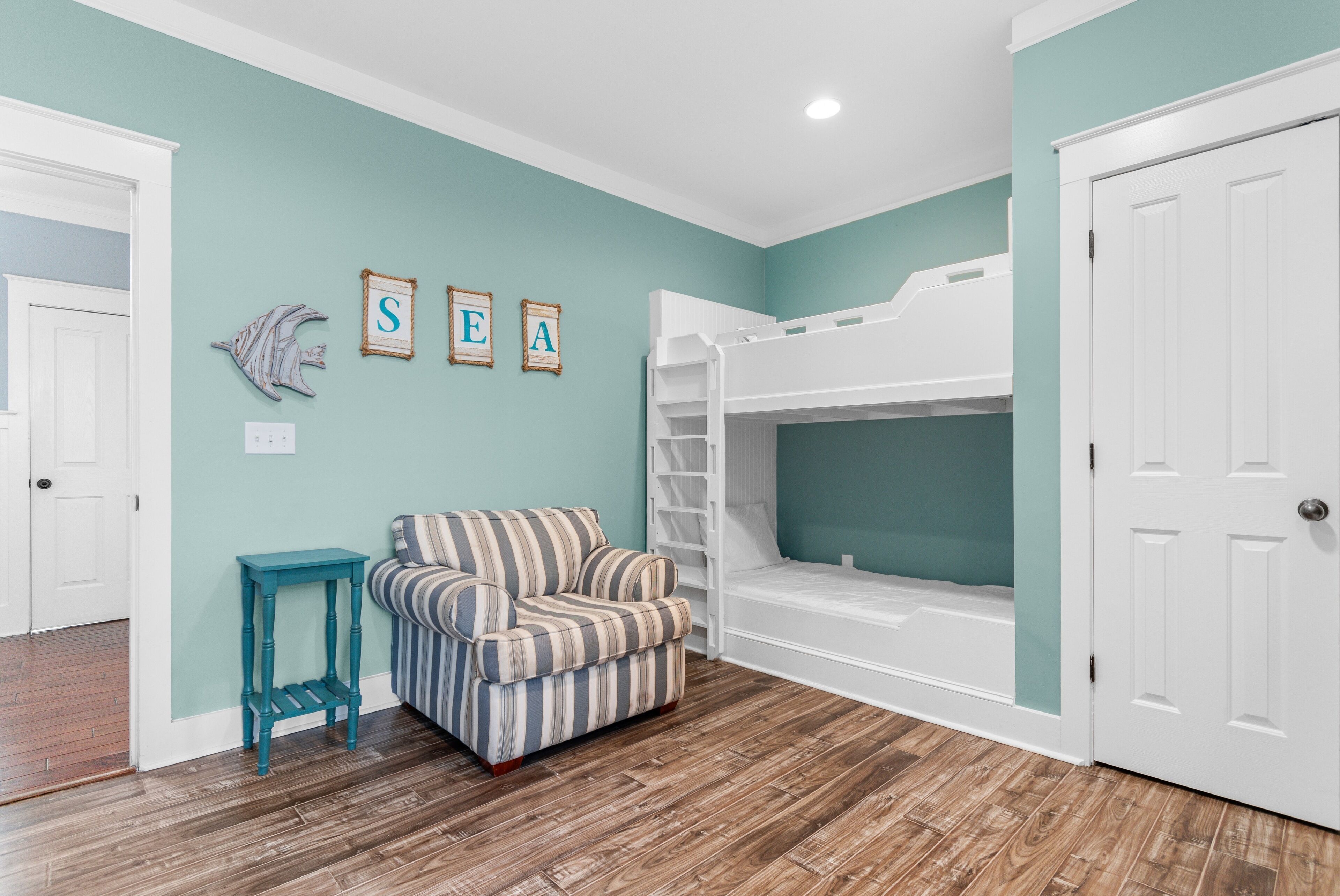 A room with teal walls, a bunk bed, a striped armchair, and a small table.