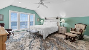 A bedroom with a bed, a chair, a nightstand, a lamp, and a ceiling fan.