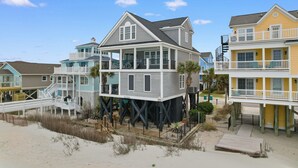 A beachfront house with a balcony, a deck, and a staircase leading to the upper floor.