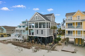 Una casa frente a la playa con balcón, terraza y una escalera que lleva al piso superior.