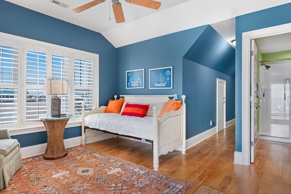 Un dormitorio con cama blanca, paredes azules y un ventanal con persianas.