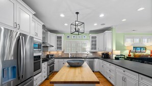 A modern kitchen with white cabinets, stainless steel appliances, a wooden island, and a hanging light fixture. - 7BR Home Near Surfside Pier w/ Private Pool & Wi-Fi (Surfside Beach)