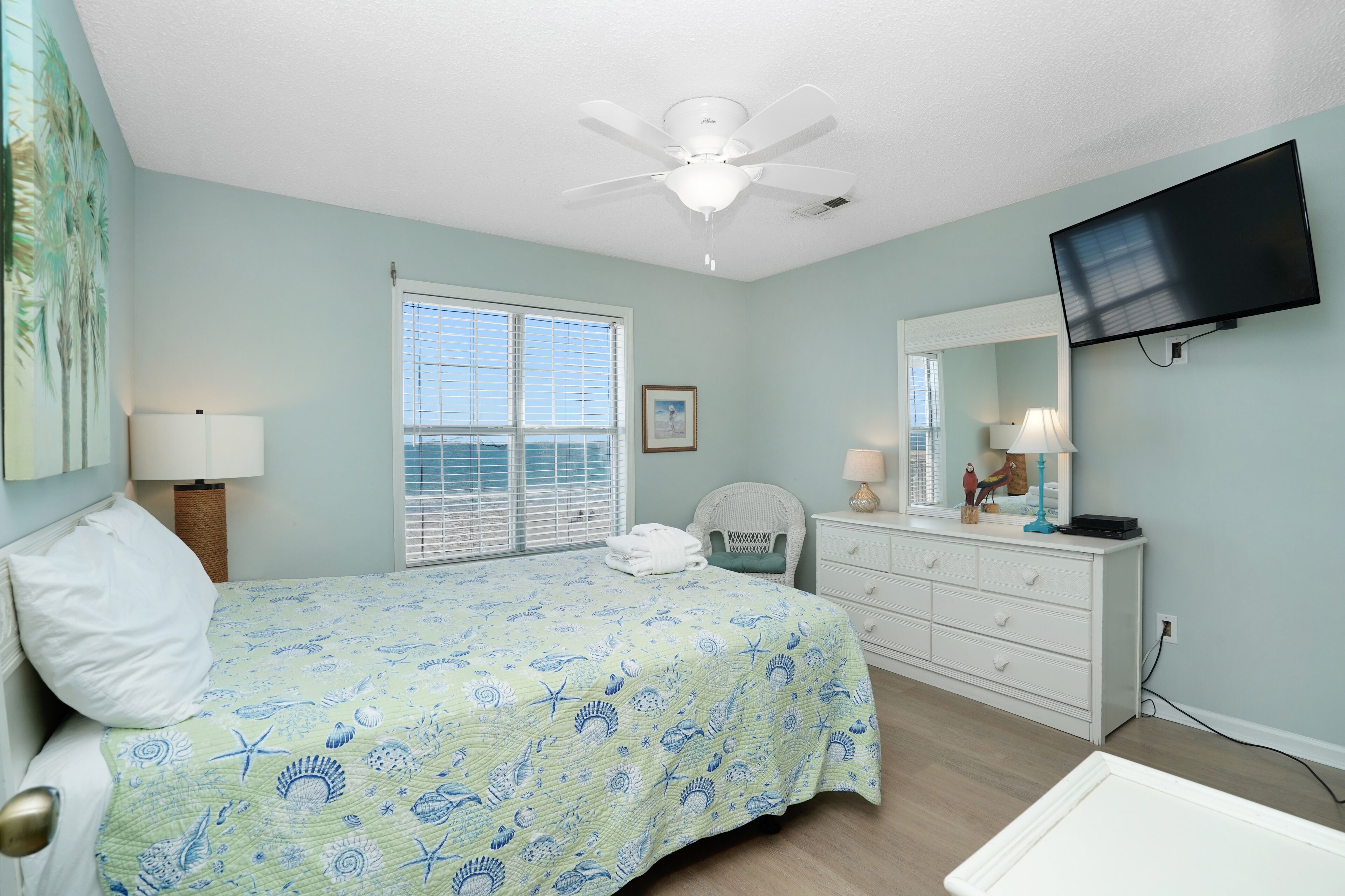 Une chambre à coucher avec un lit, un ventilateur de plafond, une télévision, une fenêtre et une commode.