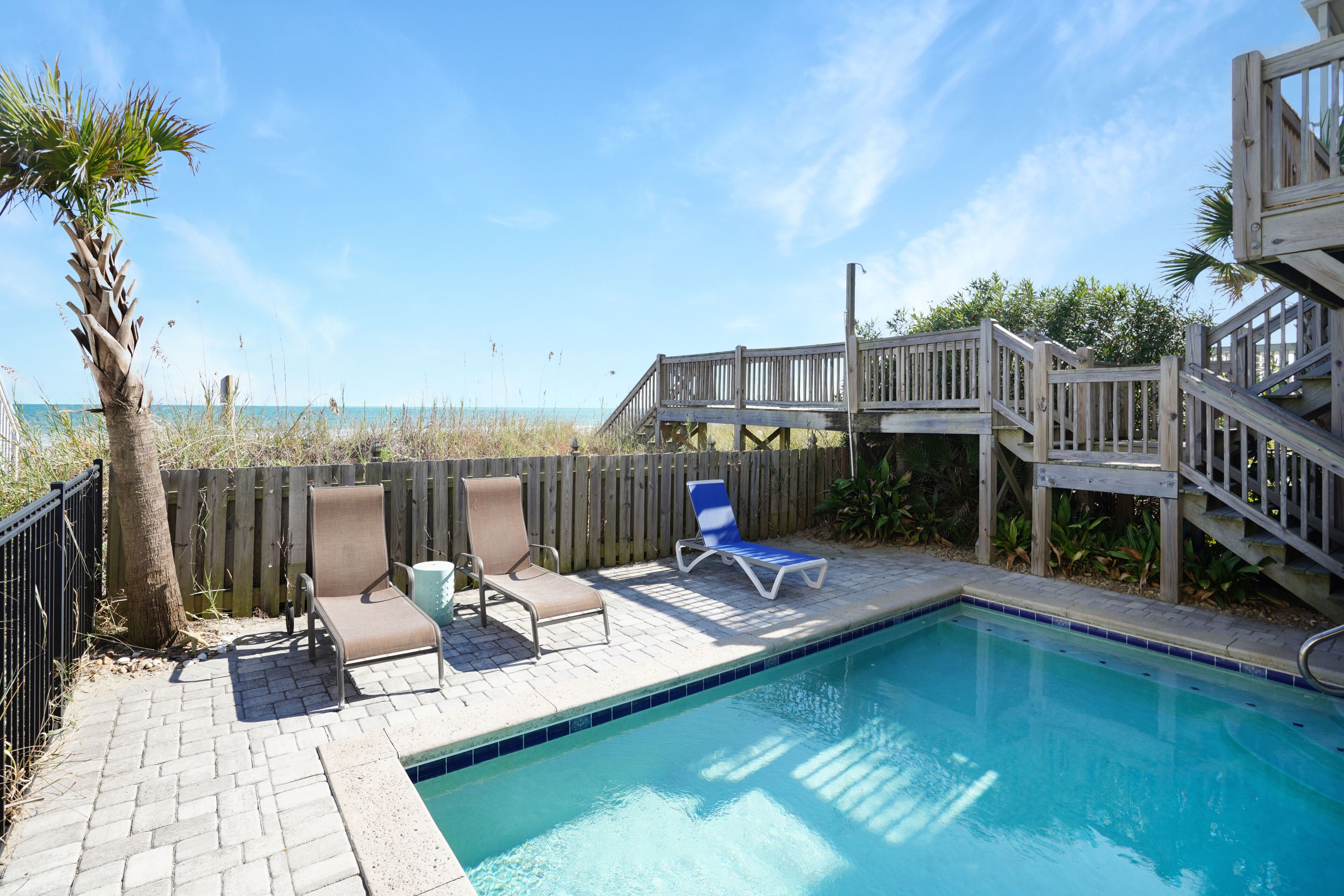 Un espace piscine doté d’une terrasse en bois, de deux chaises longues et d’un escalier en bois menant à une autre terrasse.