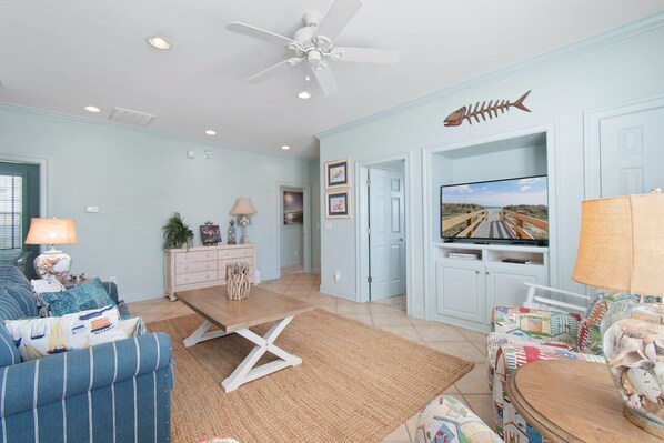 A living room with a sofa, a coffee table, a TV, and a ceiling fan. - 4BR w/ Private Pool & Beach Views Near Garden City Pier (Garden City Beach)