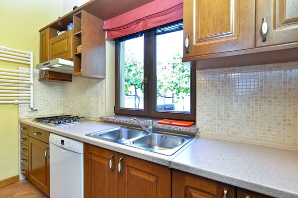 A kitchen with wooden cabinets, a double sink, and a window with a red valance.