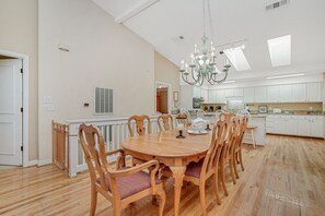 A spacious dining area with a large wooden table surrounded by chairs, a chandelier, and a view into the kitchen. - Inlet Front 5BR Home w/ Private Dock & Ocean Views (Garden City Beach)