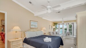 Quarto com uma cama grande, duas mesas de cabeceira com luminárias, um ventilador de teto e vista para o exterior.