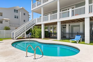 A swimming pool with a curved edge, a set of stairs leading to a balcony, and a fenced area with a chair.