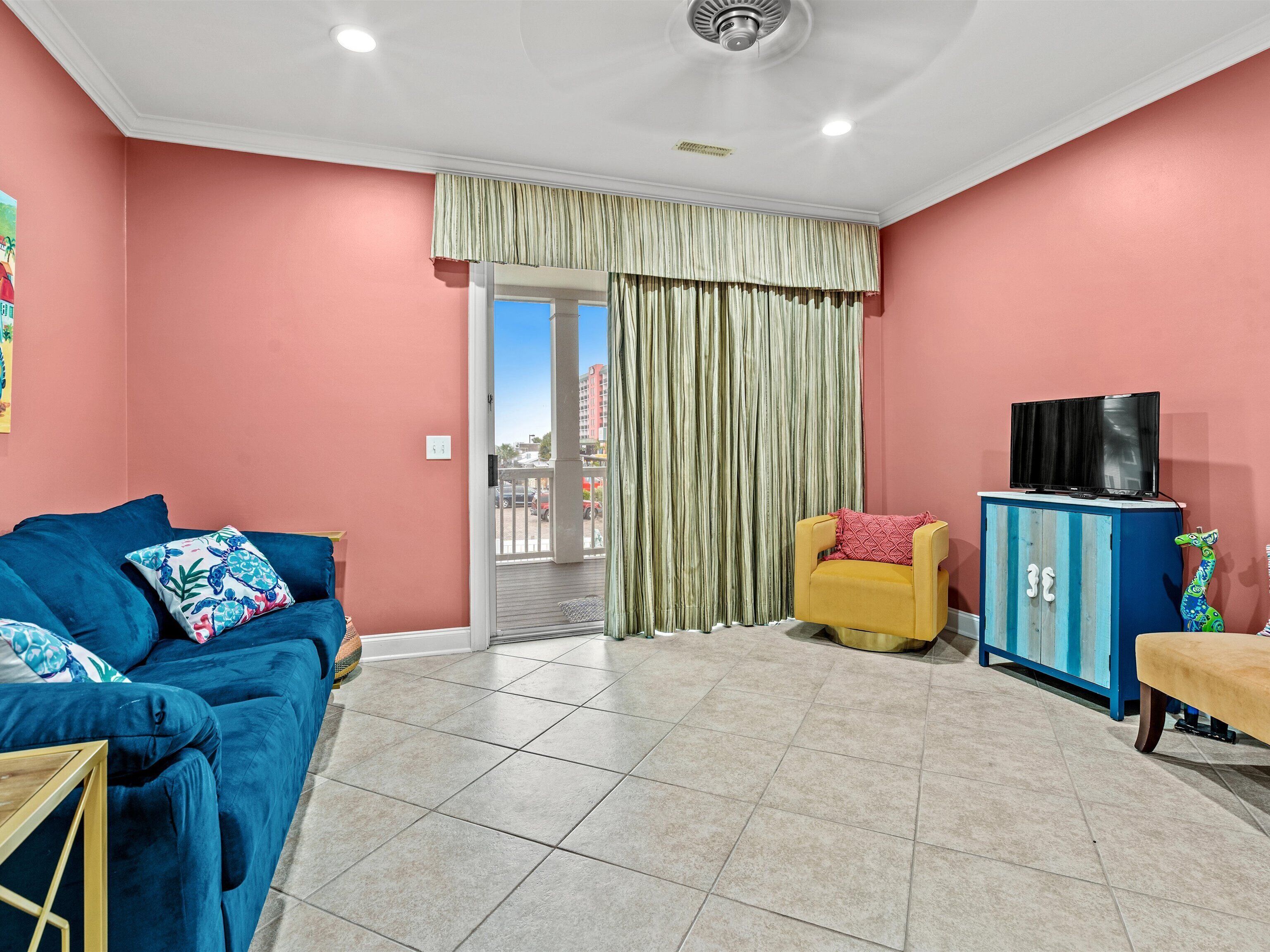 A living room with a blue sofa, a yellow armchair, a TV on a cabinet, and a view through a door.