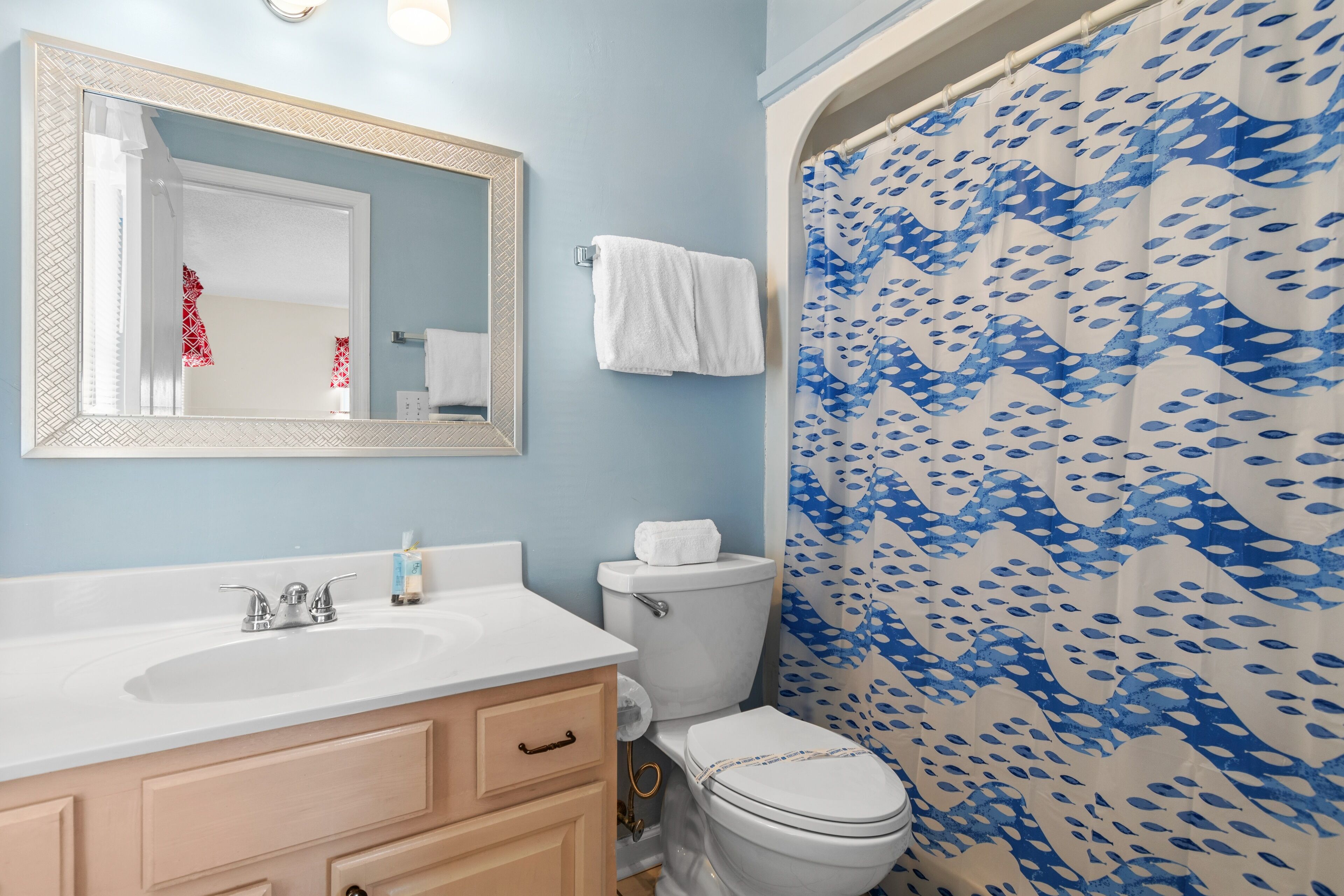 A bathroom with a white sink, a mirror, a toilet, and a shower curtain with a blue wave pattern.