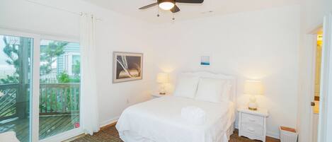 A hotel room with a bed, two bedside tables with lamps, a ceiling fan, a large window with a view of a balcony, and a framed picture on the wall.