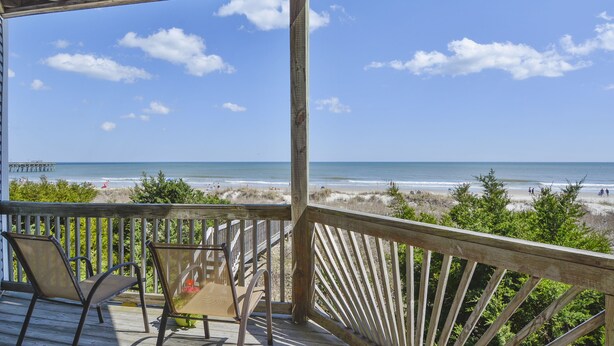 A wooden deck with chairs overlooking a beach.