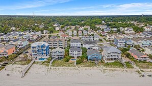A coastal residential area with houses, a beach, and a lighthouse in the distance.