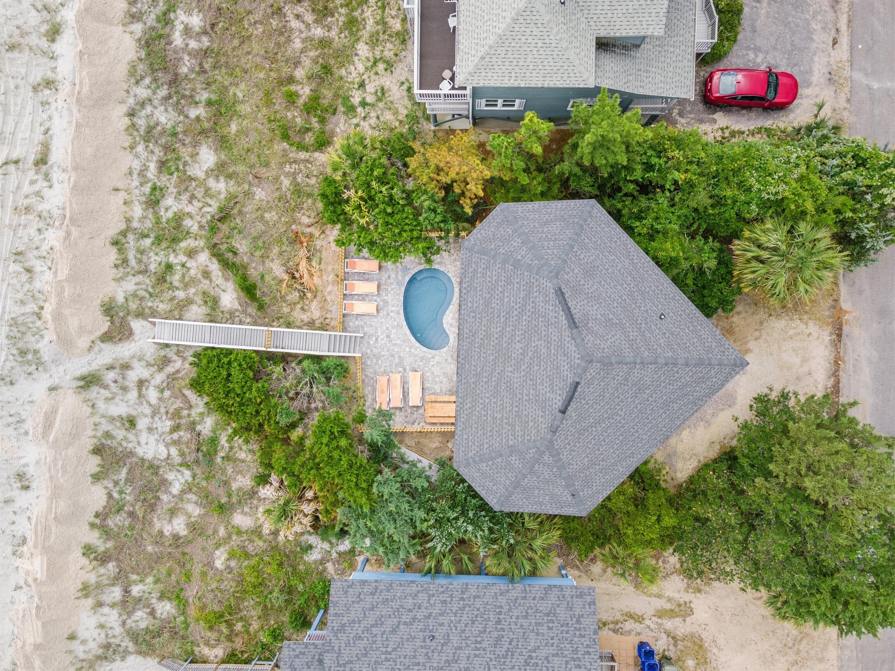An aerial view of a property with a swimming pool, a covered patio, and a red car parked on the street.