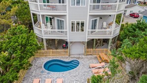 A multi-story building with a swimming pool, outdoor seating, and a wooden fence.