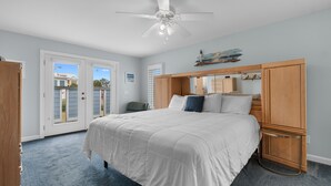 A bedroom with a bed, a ceiling fan, a wooden headboard, a nightstand, and a door leading to an outdoor area. - Inlet Front 5BR Home w/ Private Dock & Walk to Beach (Garden City Beach)
